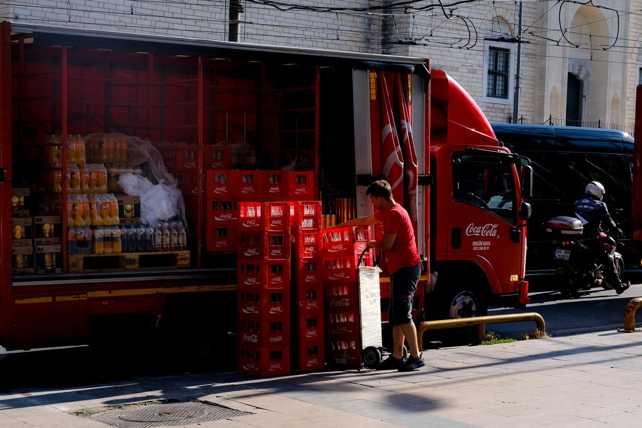 Delivery worker unloading Coca Cola crates from truck on city street, showcasing beverage supply logistics.