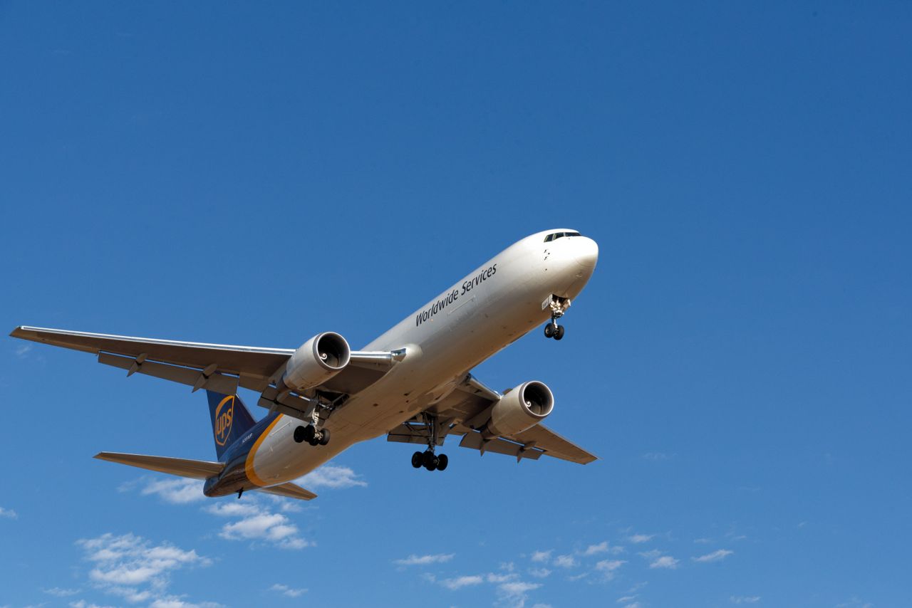 A cargo plane from a well-known logistics company flies against a vibrant blue sky.