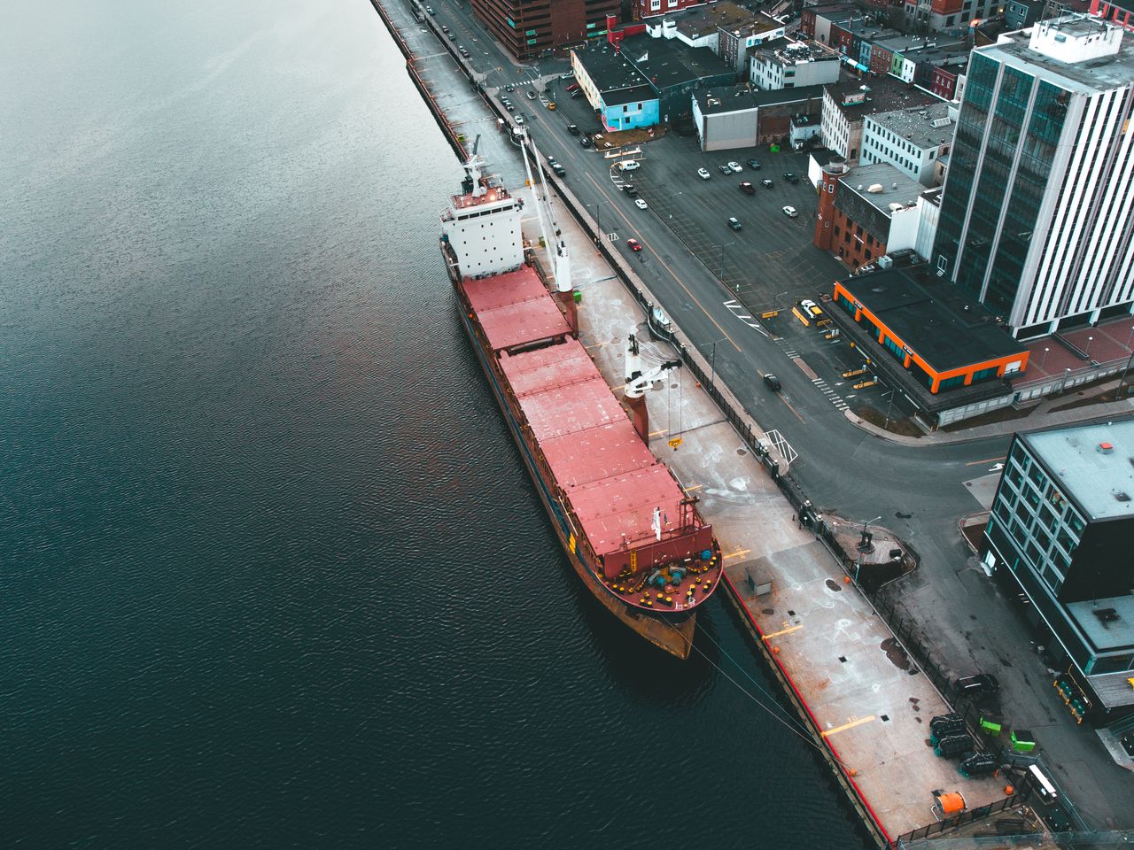 Drone view of modern dock with industrial ship moored in rippling water in daytime